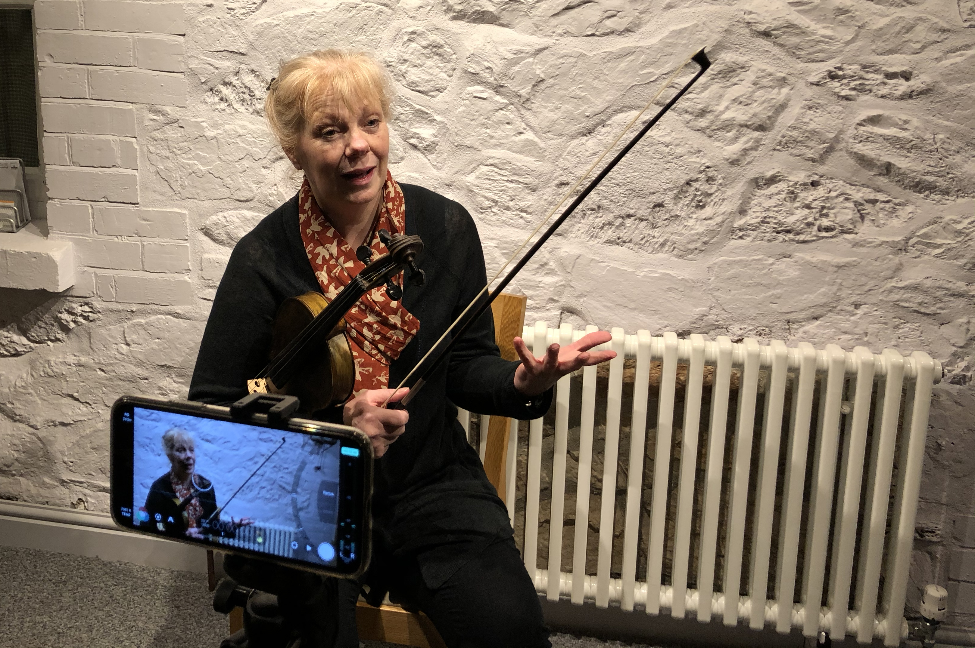 Gillian Taylor with a violin under her arm, being filmed on a mobile phone