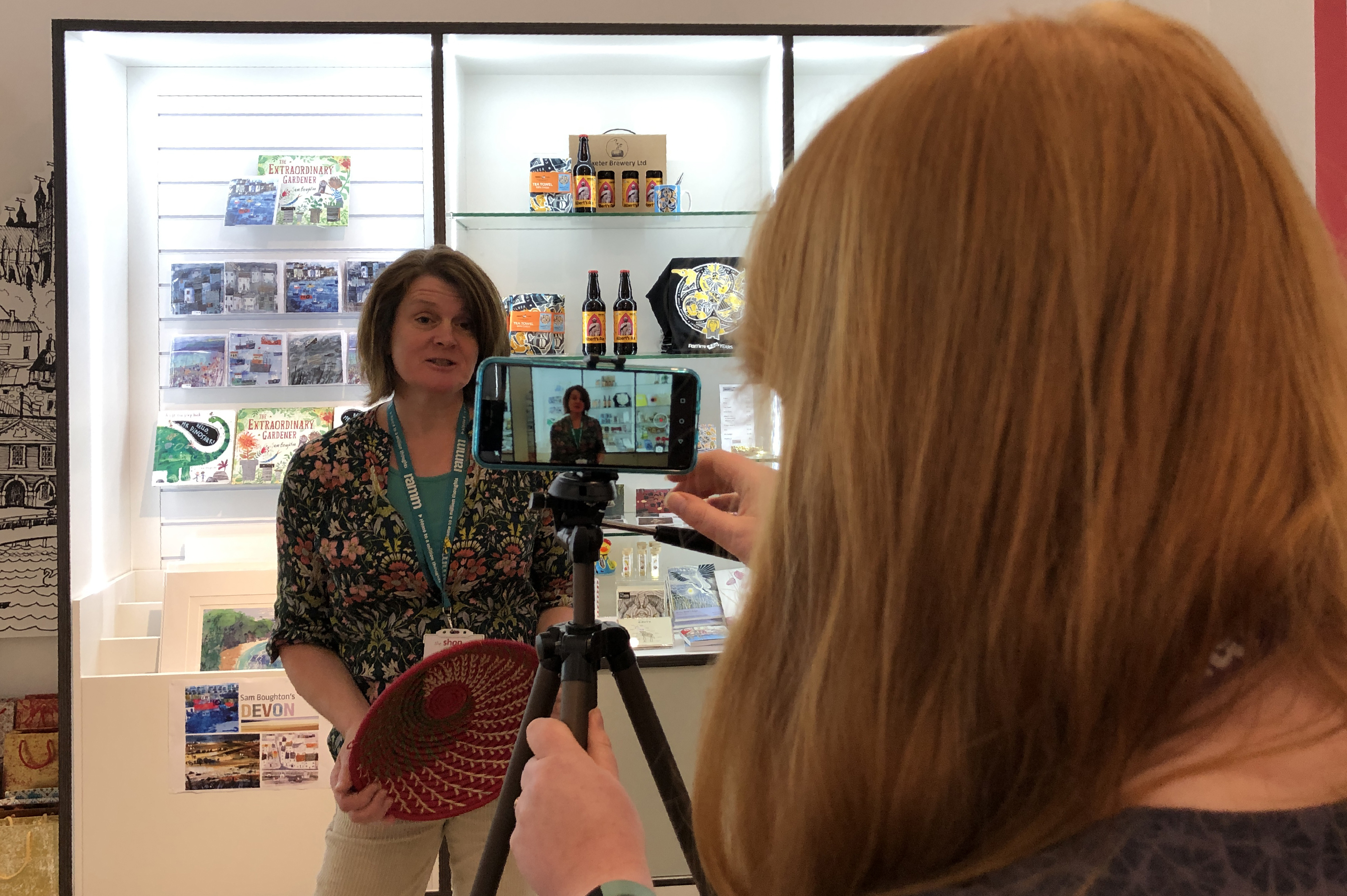 Woman filming another woman with a mobile phone on a tripod, standing in front of a display