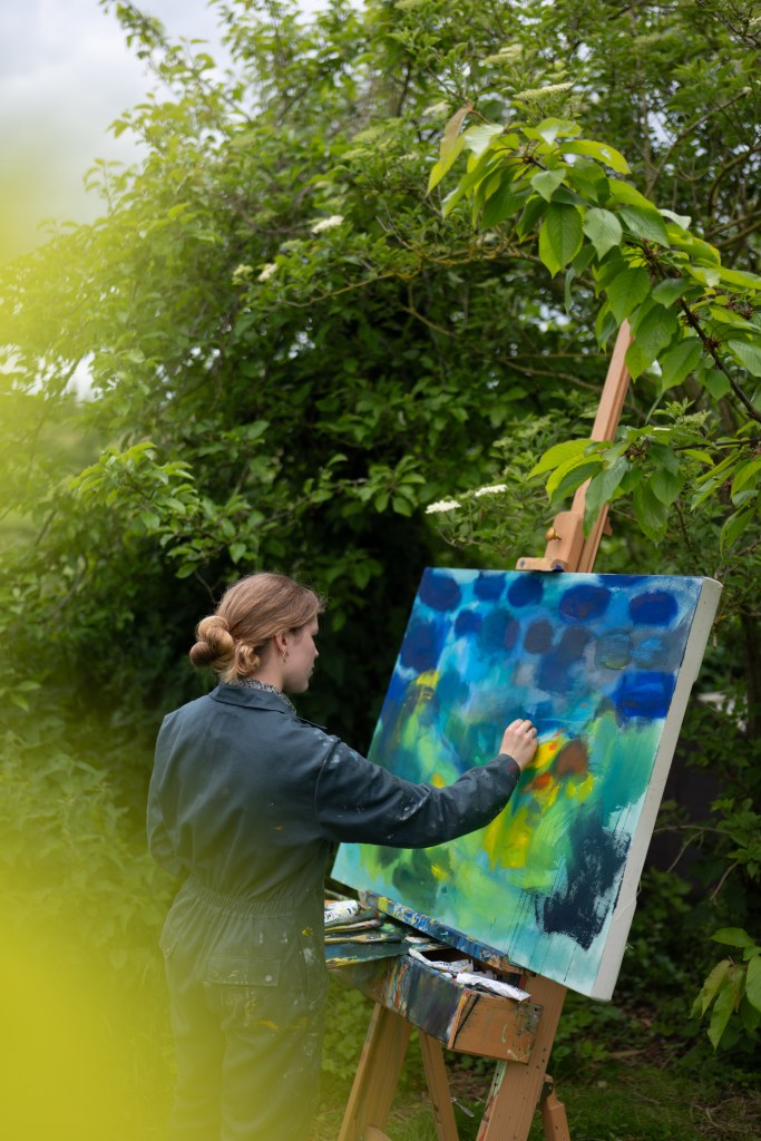 Octavia Madden amongst trees, standing in front of an easel, painting
