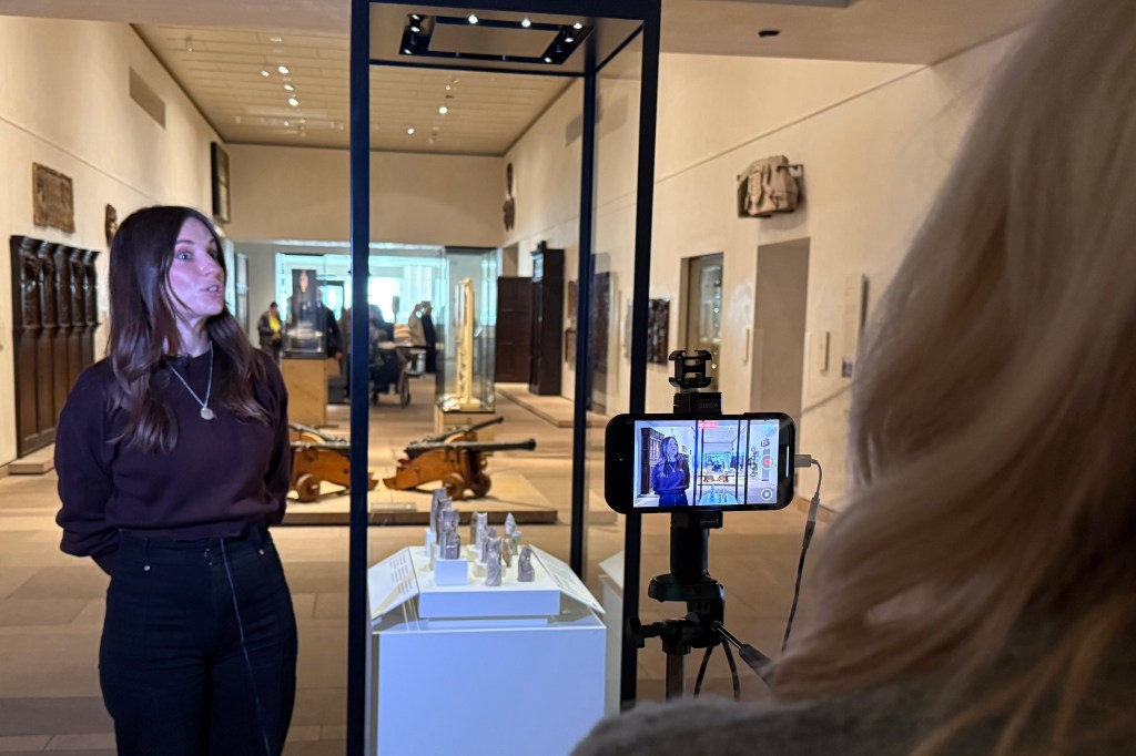 A woman being filmed next to the Lewis chess pieces in a museum